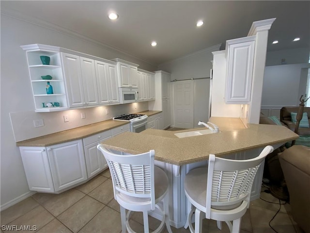 kitchen with a breakfast bar, white cabinets, kitchen peninsula, a barn door, and white appliances