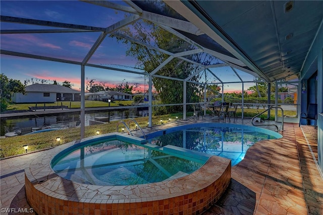 pool at dusk featuring glass enclosure, a patio area, and a pool with connected hot tub