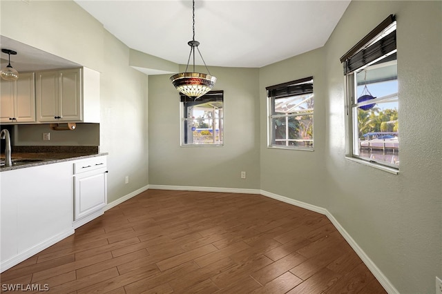 unfurnished dining area featuring dark wood-style flooring, a sink, and baseboards