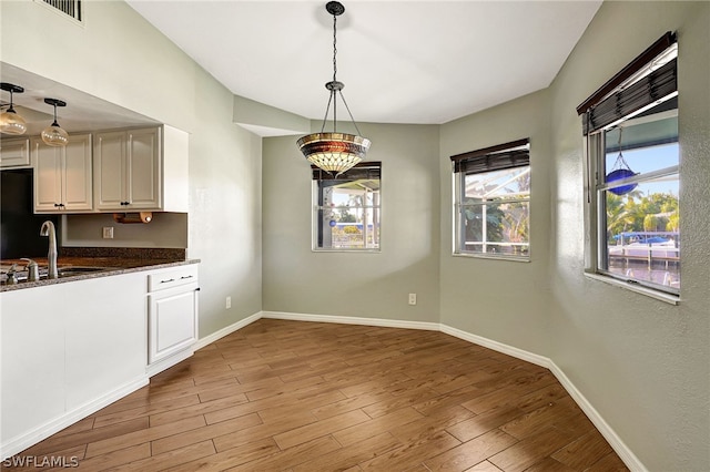 unfurnished dining area featuring visible vents, a sink, baseboards, and wood finished floors