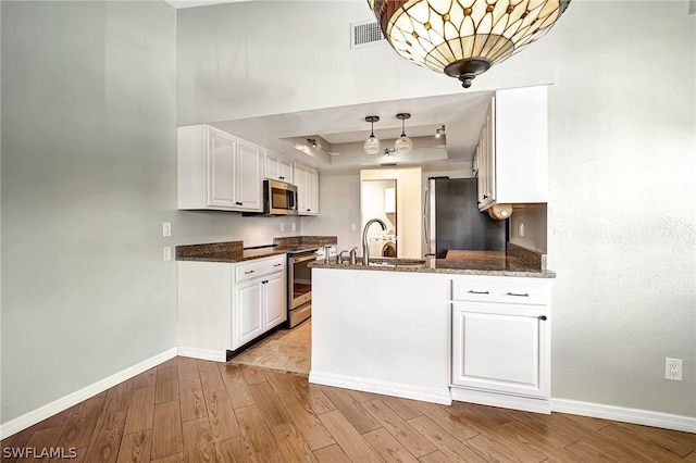 kitchen featuring baseboards, white cabinets, light wood-style floors, appliances with stainless steel finishes, and a raised ceiling