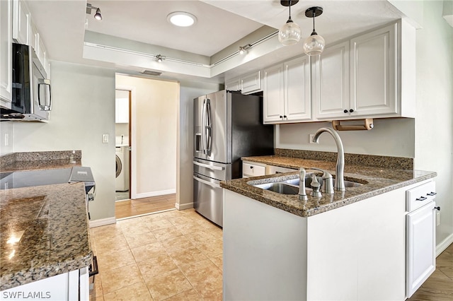 kitchen with washer / dryer, dark stone counters, appliances with stainless steel finishes, white cabinetry, and a sink