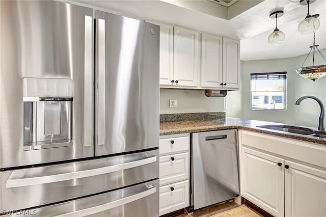 kitchen featuring decorative light fixtures, appliances with stainless steel finishes, white cabinetry, a sink, and dark stone countertops