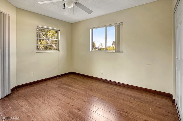 empty room featuring a healthy amount of sunlight, a textured ceiling, baseboards, and wood finished floors