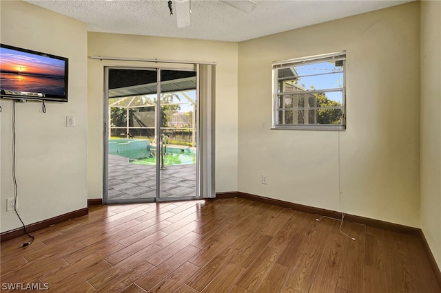 unfurnished room with a textured ceiling, wood finished floors, a sunroom, and baseboards