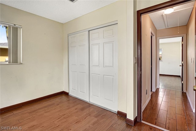 unfurnished bedroom with attic access, baseboards, wood finished floors, a textured ceiling, and a closet