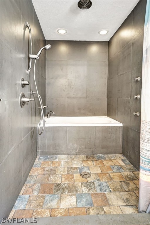 full bathroom with tile walls, tiled tub, stone finish floor, and tiled shower