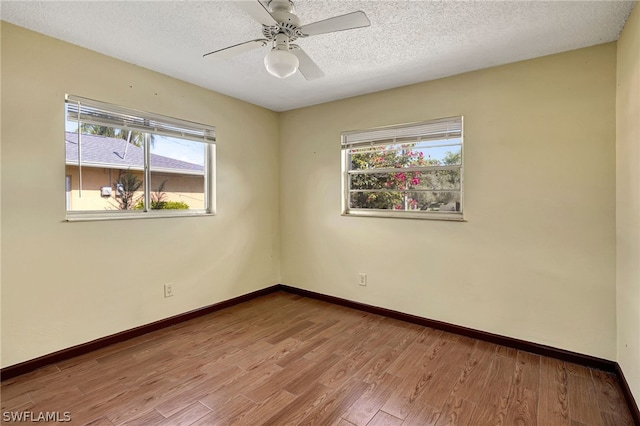 empty room with plenty of natural light, a textured ceiling, baseboards, and wood finished floors