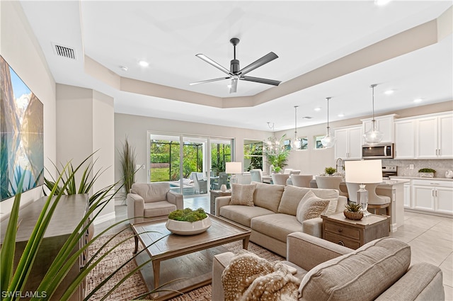 tiled living room with ceiling fan and a raised ceiling