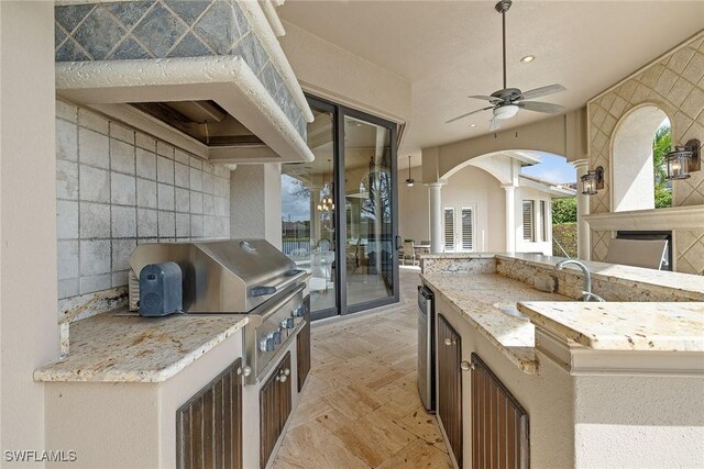 kitchen featuring ceiling fan, light stone countertops, sink, and tile walls