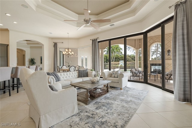 living room featuring ornamental molding, light tile patterned flooring, a tray ceiling, and ceiling fan with notable chandelier