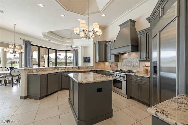 kitchen with a kitchen island, high quality appliances, custom range hood, kitchen peninsula, and decorative light fixtures