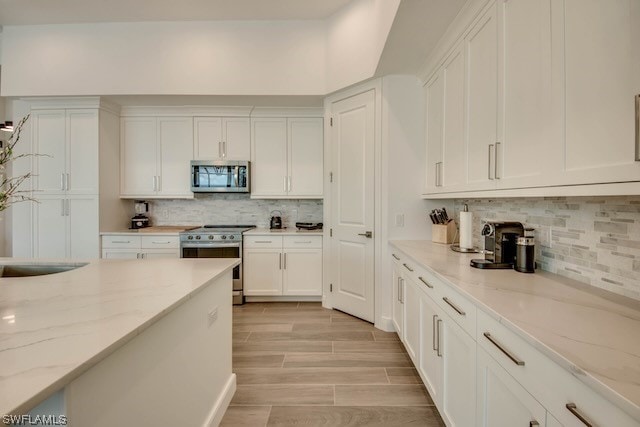 kitchen featuring light stone counters, white cabinets, appliances with stainless steel finishes, and light wood-type flooring