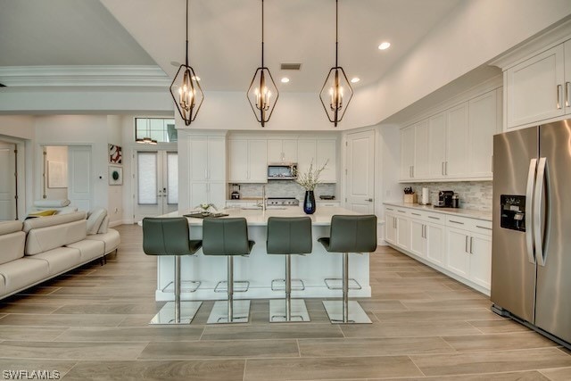 kitchen with a kitchen island with sink, white cabinetry, hanging light fixtures, light hardwood / wood-style flooring, and stainless steel appliances