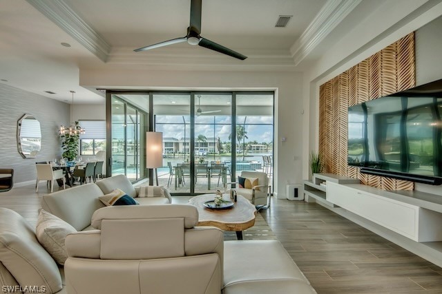 living room featuring ceiling fan with notable chandelier, a raised ceiling, ornamental molding, and hardwood / wood-style flooring