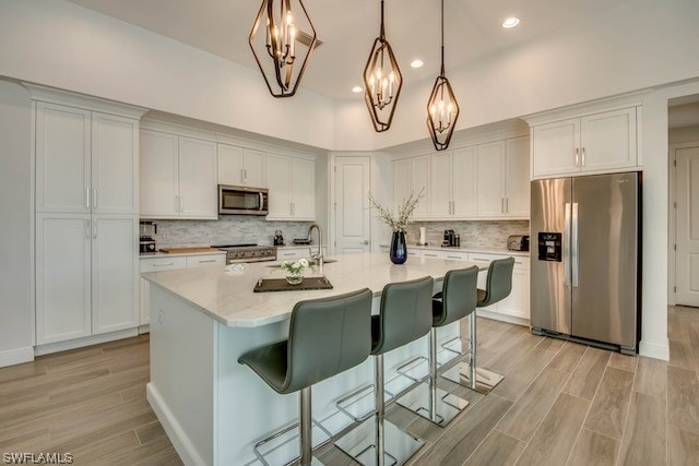 kitchen featuring appliances with stainless steel finishes, white cabinets, decorative light fixtures, a kitchen island with sink, and a notable chandelier