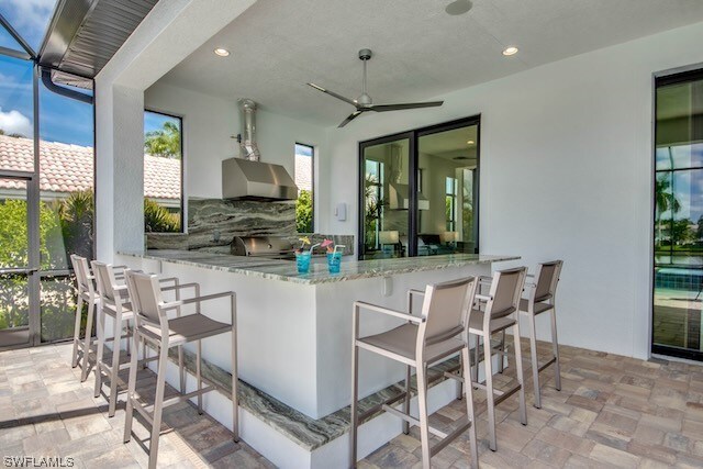 kitchen featuring decorative backsplash, wall chimney exhaust hood, kitchen peninsula, light stone countertops, and ceiling fan