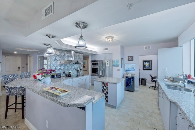 kitchen featuring a center island, decorative light fixtures, wall chimney range hood, backsplash, and sink