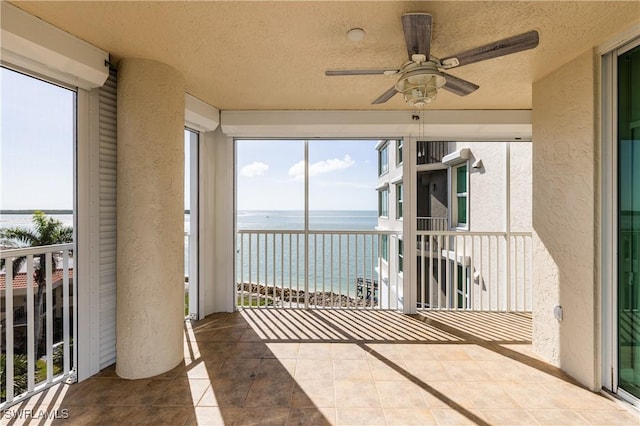 unfurnished sunroom featuring a water view, ceiling fan, and plenty of natural light