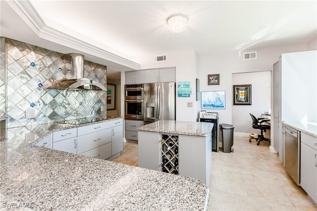 kitchen with wall chimney range hood, appliances with stainless steel finishes, gray cabinetry, a center island, and light stone counters