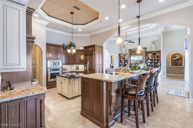 kitchen featuring decorative light fixtures, a spacious island, a tray ceiling, crown molding, and built in appliances