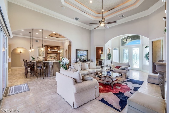 living room with ornamental molding, light tile flooring, ceiling fan, and a raised ceiling