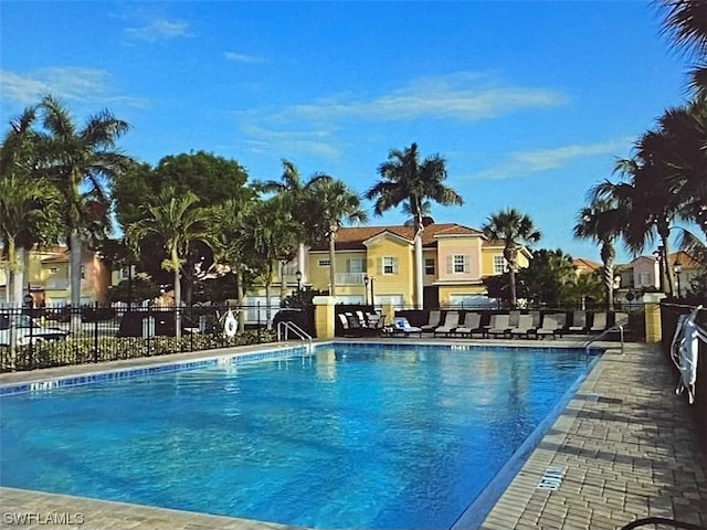 community pool with a patio area, fence, and a residential view