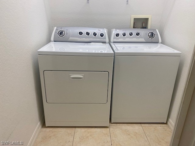 washroom with laundry area, light tile patterned flooring, baseboards, and washing machine and clothes dryer