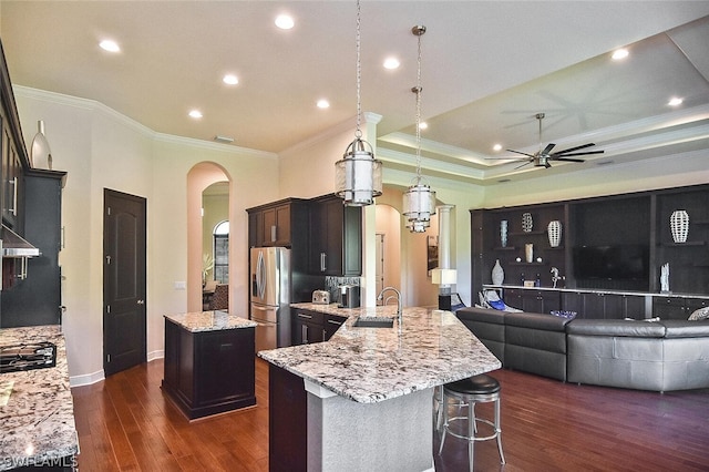 kitchen with dark hardwood / wood-style floors, an island with sink, ceiling fan, and light stone countertops