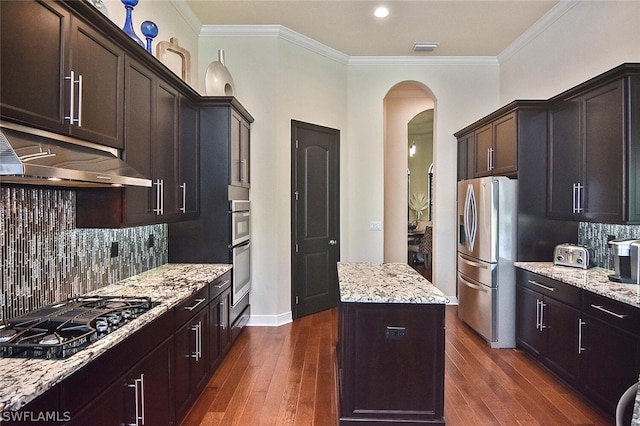 kitchen with appliances with stainless steel finishes, a kitchen island, tasteful backsplash, and dark wood-type flooring