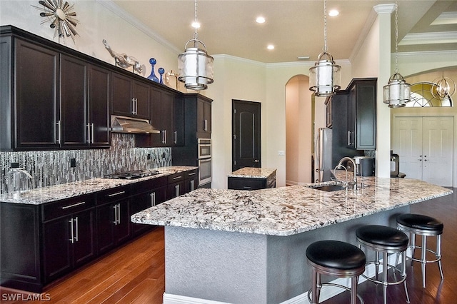 kitchen featuring crown molding, backsplash, dark wood-type flooring, and an island with sink