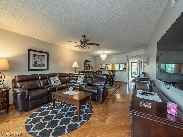 living room featuring a textured ceiling, light wood-type flooring, and ceiling fan