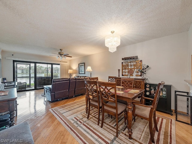 dining room with light wood-style flooring, a textured ceiling, and ceiling fan with notable chandelier