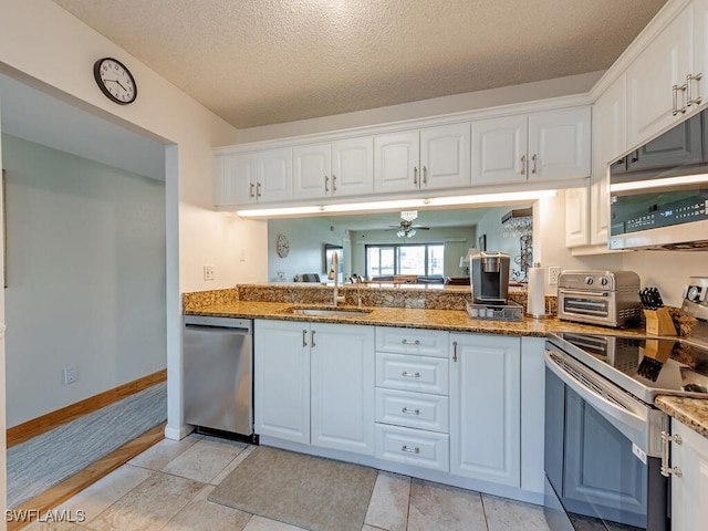 kitchen featuring a textured ceiling, a sink, white cabinets, appliances with stainless steel finishes, and dark stone counters