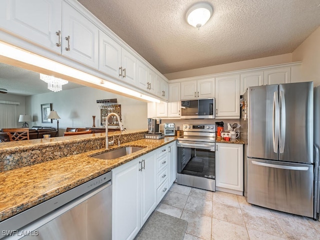 kitchen featuring appliances with stainless steel finishes, white cabinets, a sink, a textured ceiling, and light stone countertops