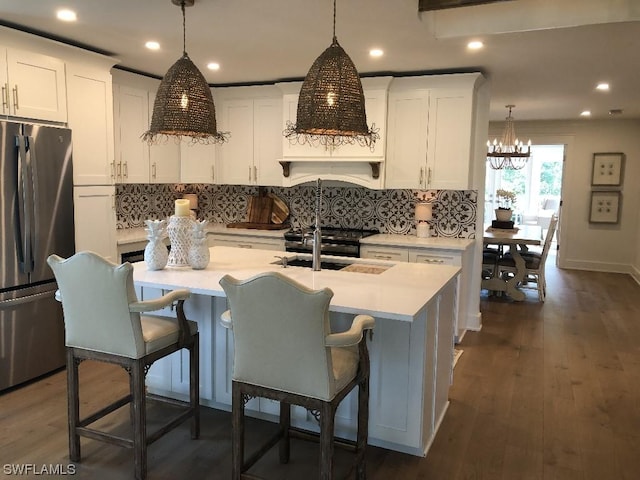 kitchen with stainless steel fridge, a center island with sink, and white cabinets