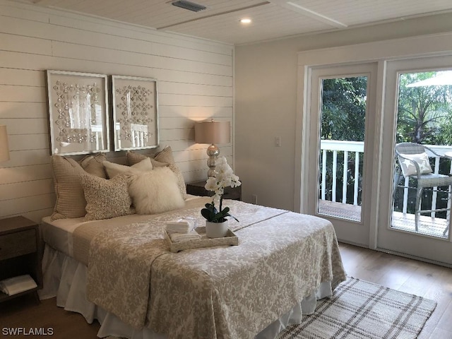 bedroom with wooden walls, hardwood / wood-style flooring, and access to outside