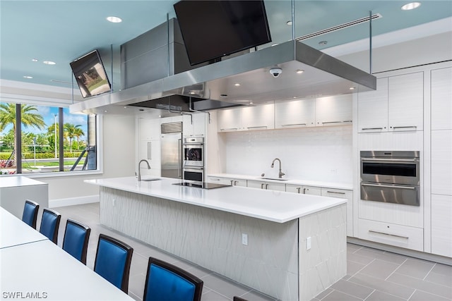 kitchen with light countertops, a kitchen island with sink, a kitchen bar, and modern cabinets