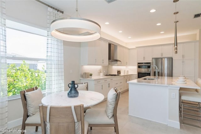 kitchen with stainless steel appliances, white cabinets, hanging light fixtures, and wall chimney exhaust hood