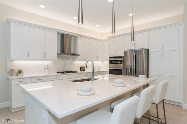 kitchen with stainless steel appliances, hanging light fixtures, a sink, wall chimney range hood, and light stone countertops