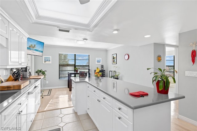 kitchen with light tile floors, crown molding, a kitchen island, a tray ceiling, and white cabinetry