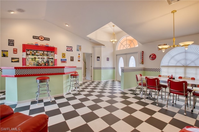 interior space with decorative light fixtures, a notable chandelier, dark tile floors, a kitchen bar, and vaulted ceiling