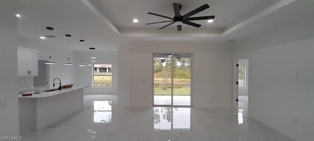 unfurnished living room with light tile flooring, a raised ceiling, ceiling fan, and sink