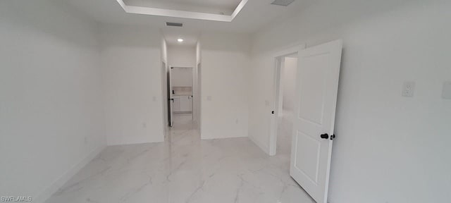 hall with a raised ceiling and light tile flooring