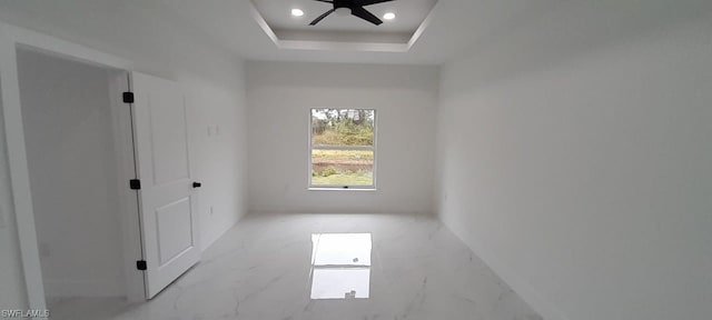 tiled spare room featuring ceiling fan and a tray ceiling