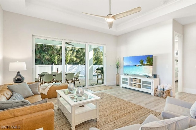 living room featuring a tray ceiling, baseboards, wood finished floors, and a ceiling fan
