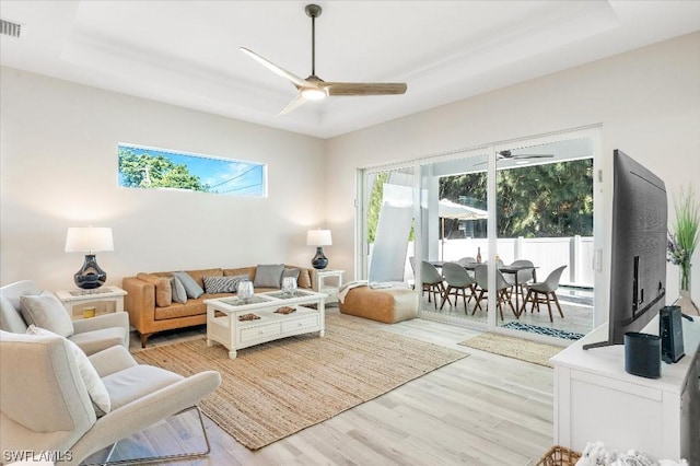 living room featuring light wood finished floors, visible vents, a ceiling fan, and a tray ceiling