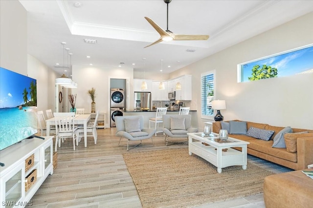 living room with a raised ceiling, crown molding, stacked washer and clothes dryer, and light wood finished floors