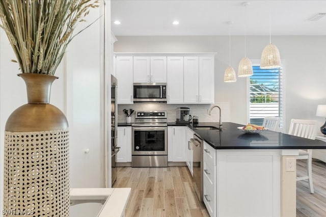 kitchen featuring dark countertops, tasteful backsplash, appliances with stainless steel finishes, a peninsula, and a sink