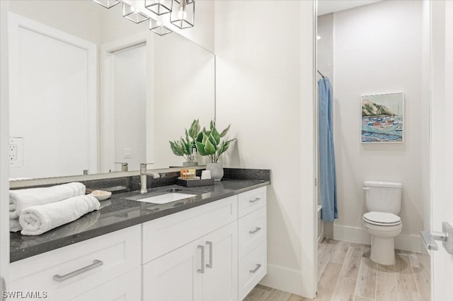 bathroom with toilet, wood finished floors, shower / tub combo, baseboards, and vanity